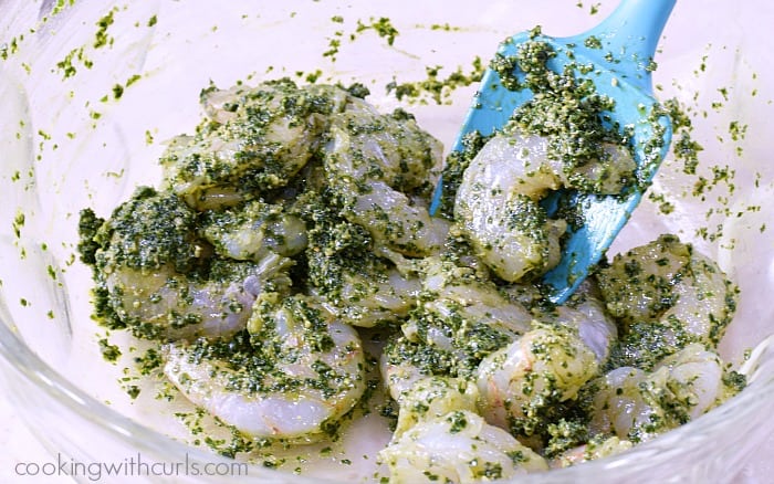 Shrimp mixed with pesto sauce in a large bowl.