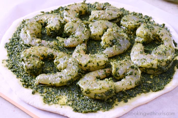 Pizza dough circle topped with pesto sauce and pesto covered shrimp.