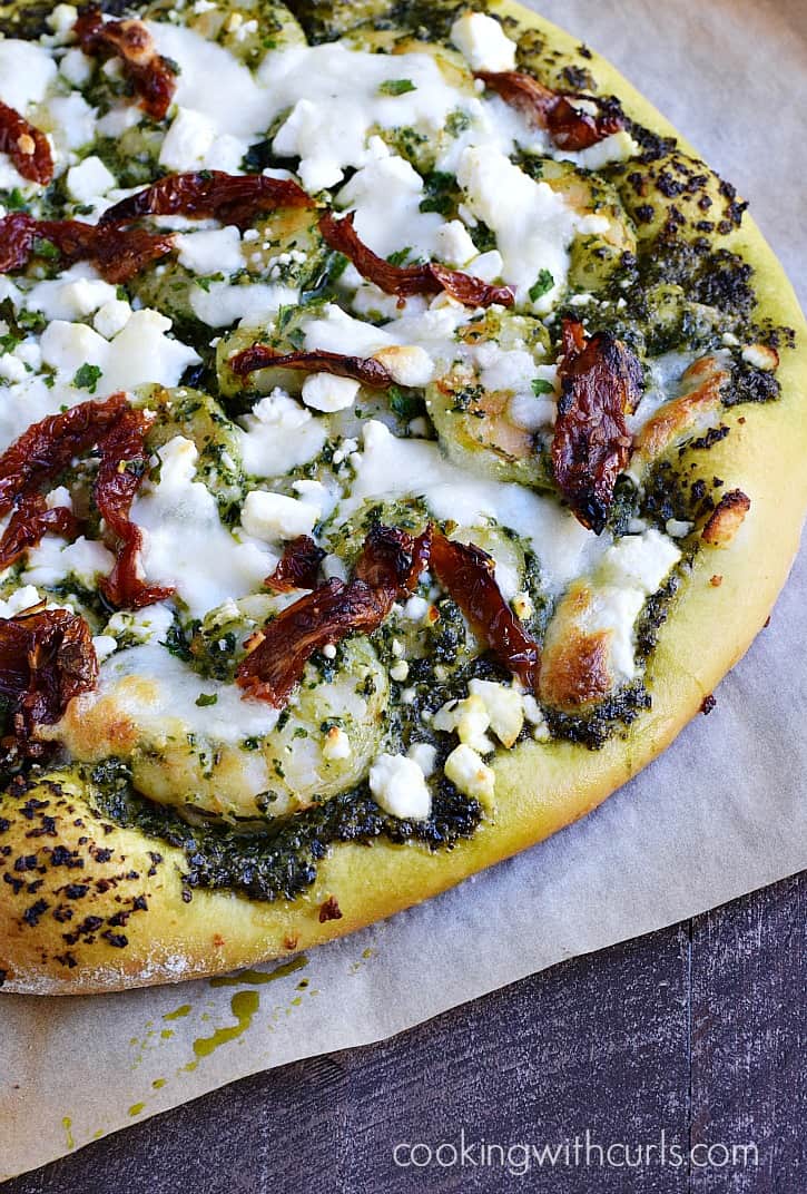 Pizza topped with pesto, shrimp, feta cheese, and sun-dried tomatoes.