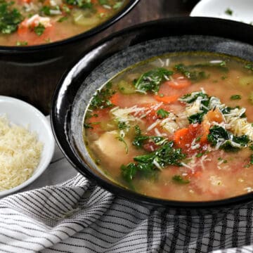 Two bowls of chunky chicken and rice soup with carrots, tomato, kale, and grated parmesan.