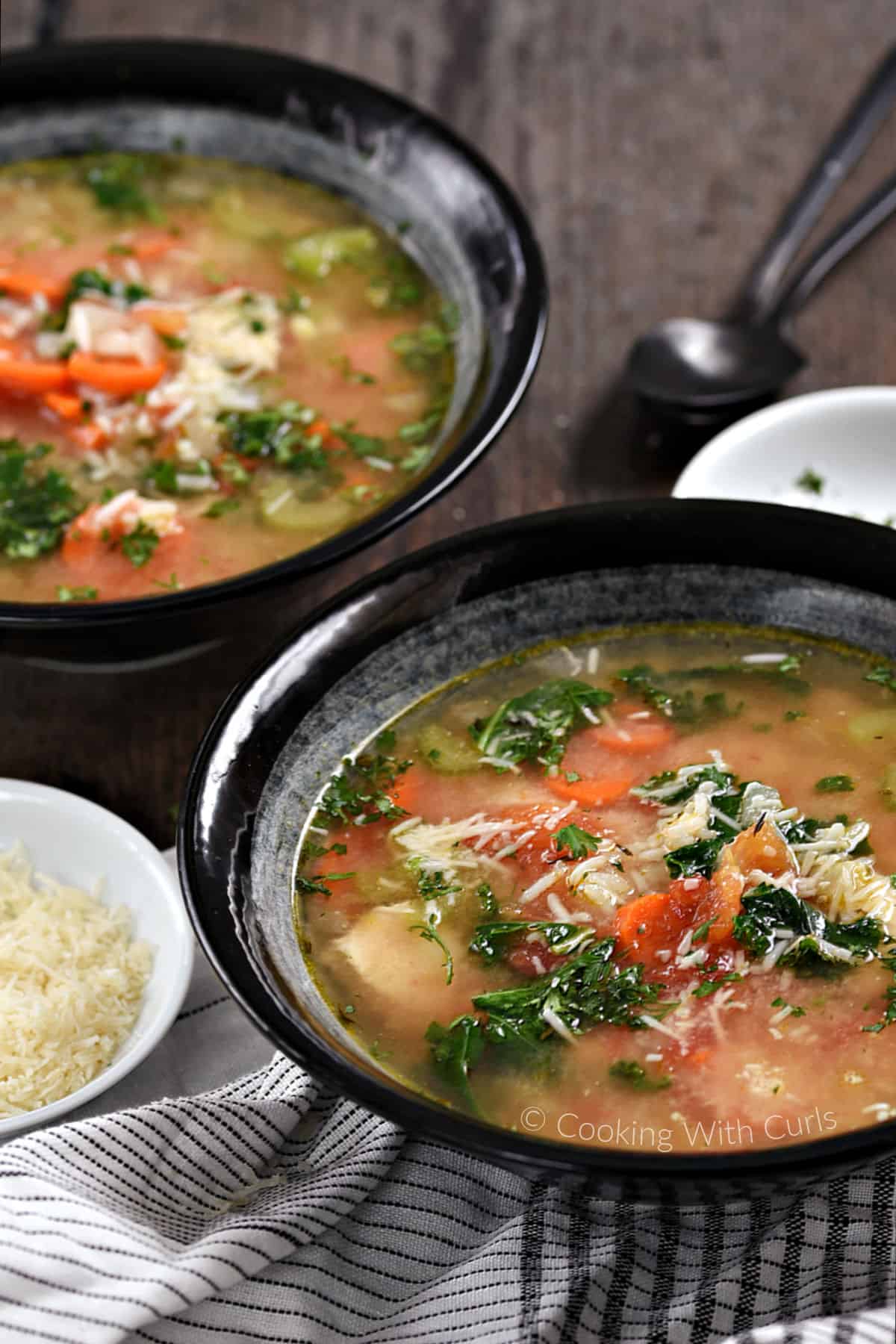 Two bowls of chunky chicken and rice soup with carrots, tomato, kale, and grated parmesan. 