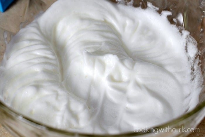 Egg whites beaten to form stiff peaks in a large mixing bowl.