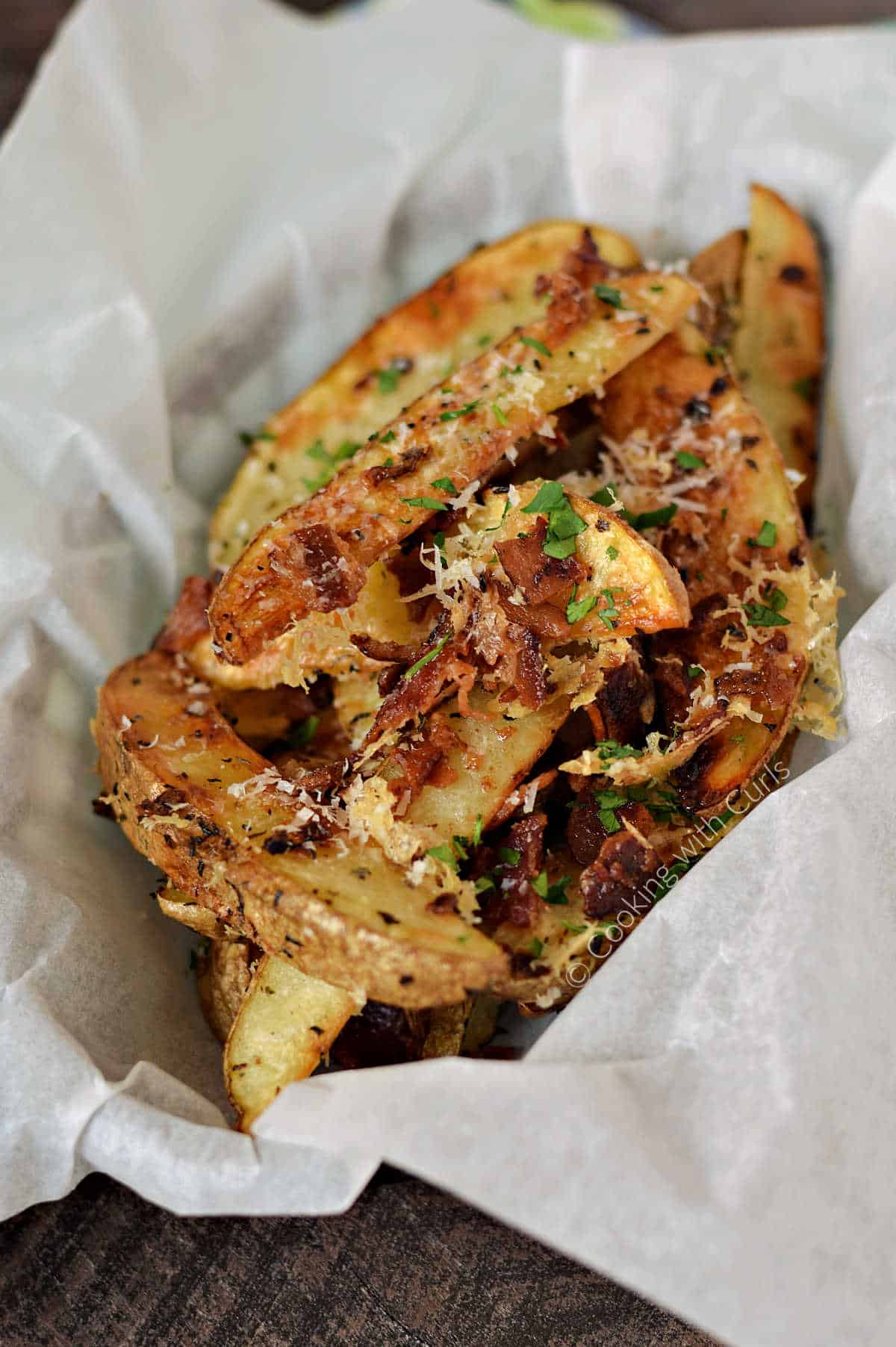 Baked potato wedges topped with Parmesan cheese, bacon, and herbs in a parchment lined basket.