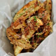 Baked potato wedges topped with Parmesan cheese, bacon, and herbs in a parchment lined basket.