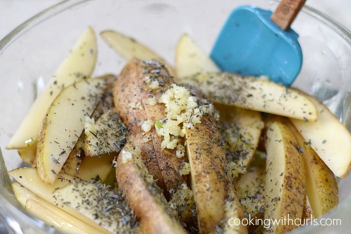 Potato wedges with garlic, oil, and herbs in a large bowl.