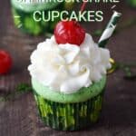 Two green cupcakes topped with white frosting, cherry and green and white striped straw with a dark green cupcake liner with light green shamrocks.