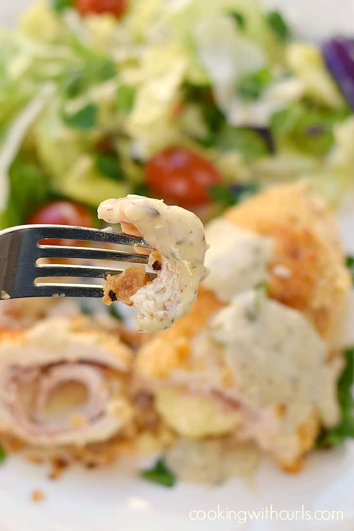 a black fork holding a piece of chicken cordon bleu above the plate with the remaining chicken and a tossed salad
