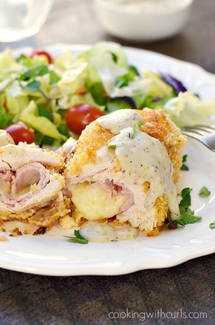 panko crusted chicken rolled around ham and cheese, but in half and sitting on a white plate with a tossed salad