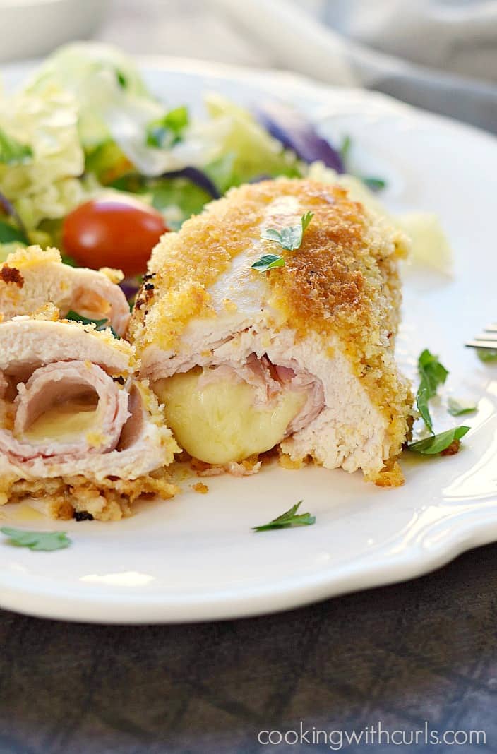 chicken cordon bleu cut in half on a white plate with a tossed salad 