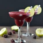 two Frozen Blackberry Margaritas in margarita glasses garnished with lime wheels and striped straws