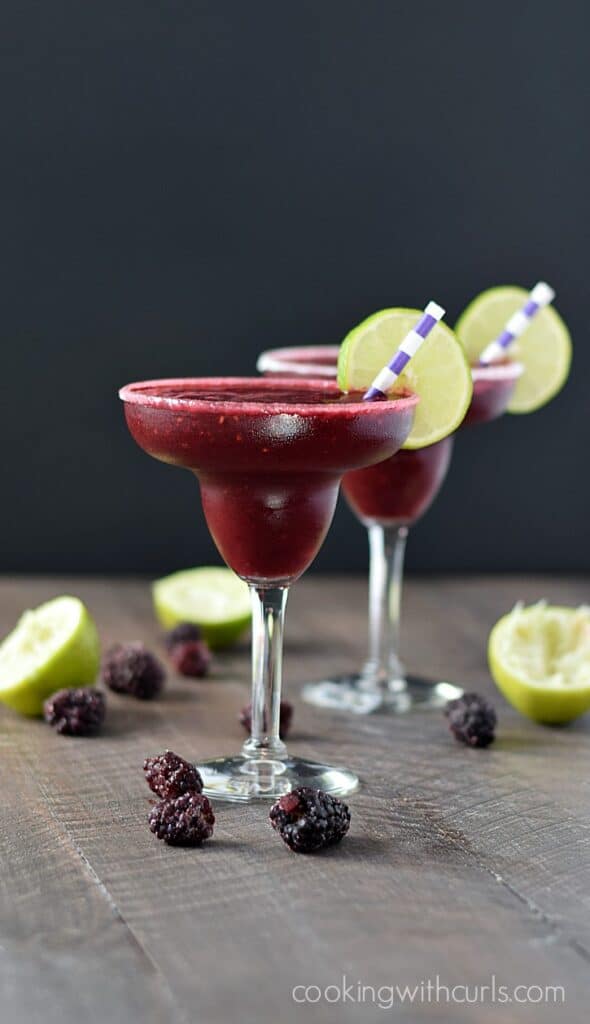 two Frozen Blackberry Margaritas in margarita glasses garnished with lime wheels and striped straws