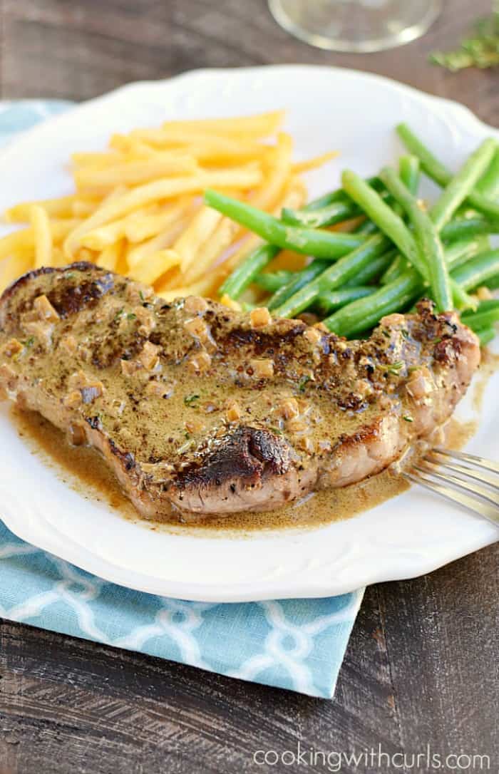 steak with french fries and green beans on a large white plate that is sitting on a blue napkin