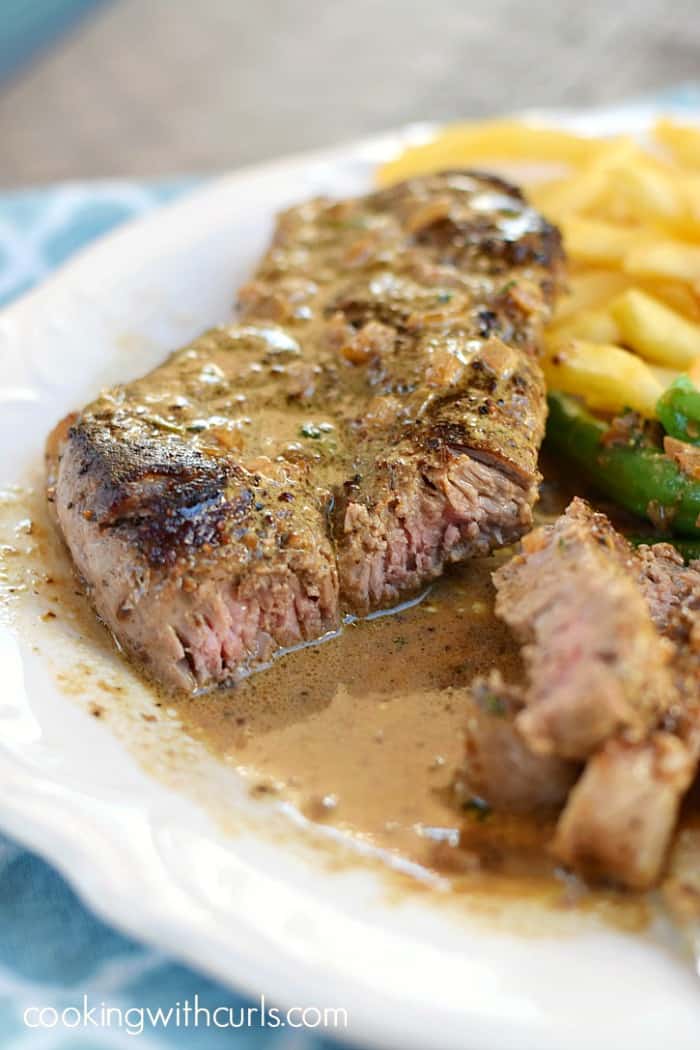 a juicy steak cut in half on a large white plate with french fries on the side