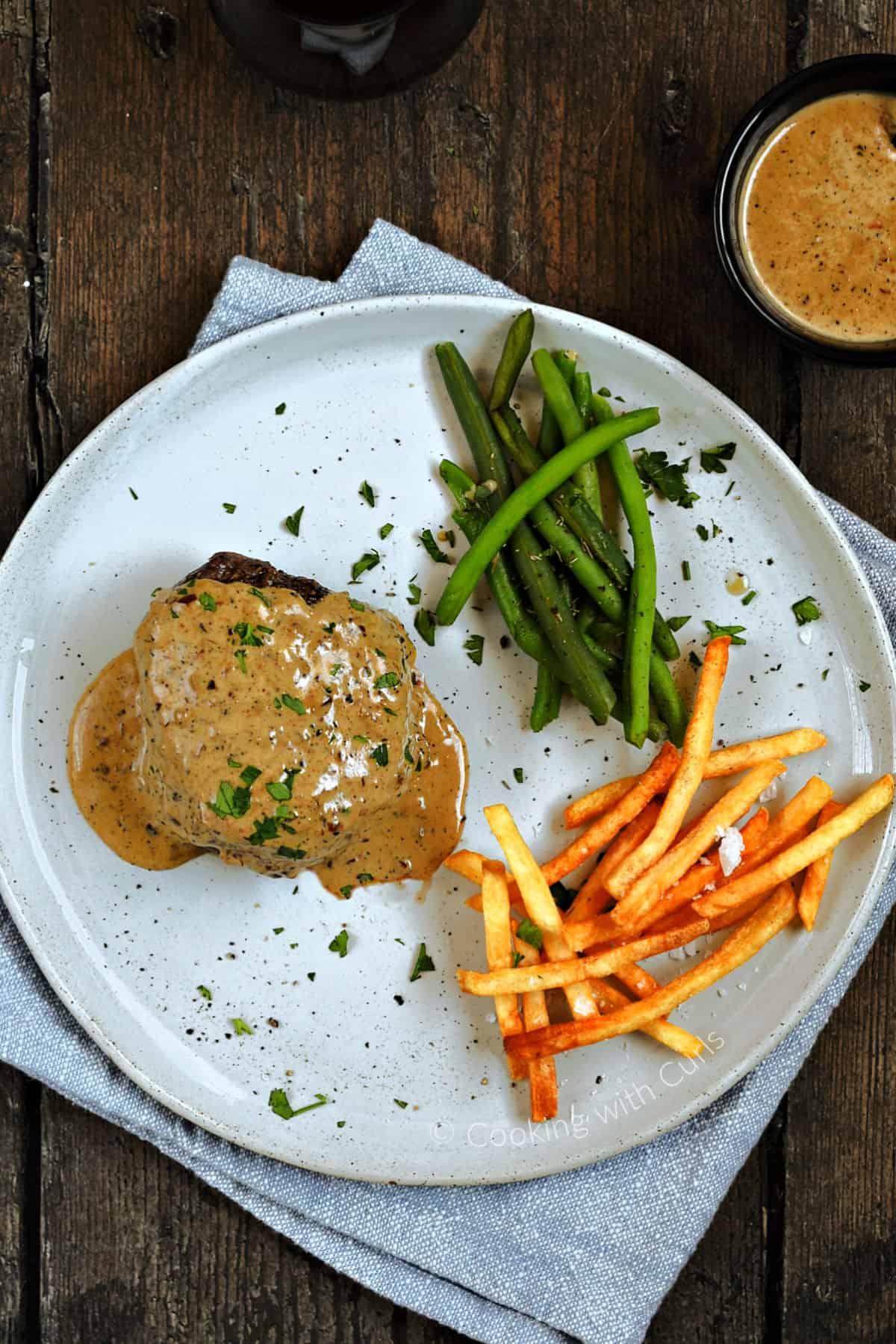 Looking down on a cream sauce covered filet mignon served on a plate with green beans and french fries.