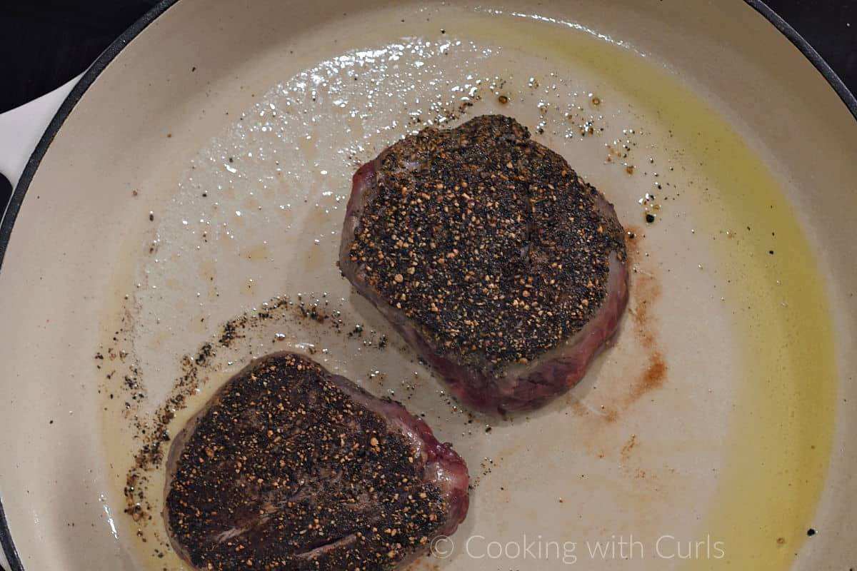 Two pepper crusted filet mignon in a skillet with olive oil. 