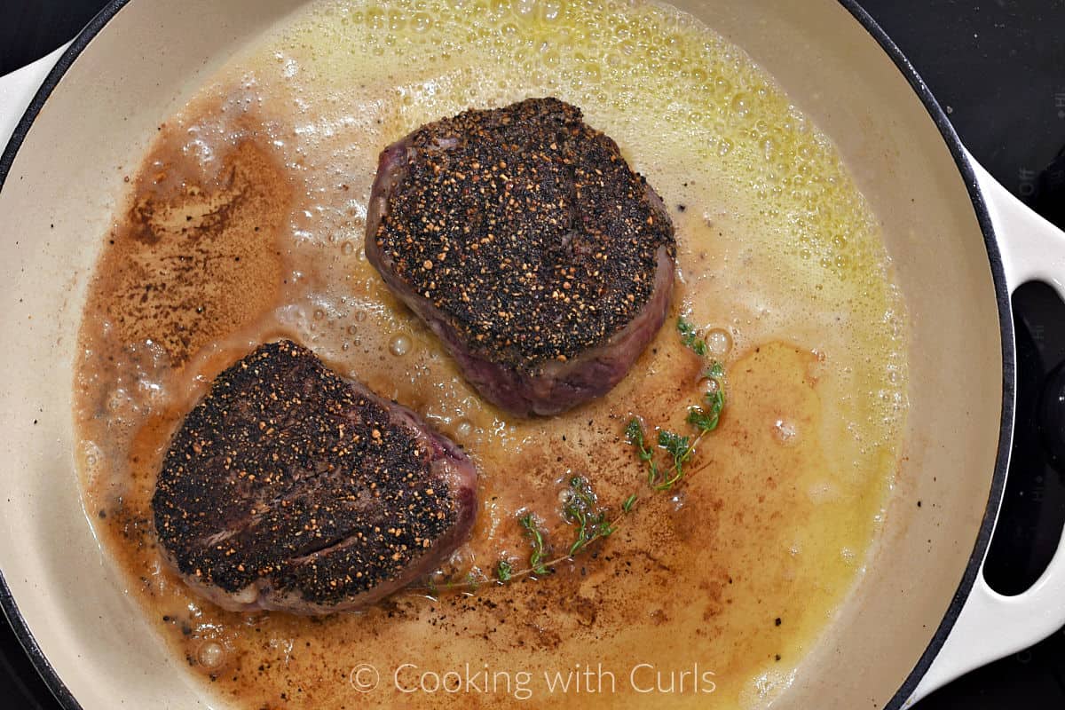 Two pepper crusted filets in a skillet with melted butter and a thyme sprig. 