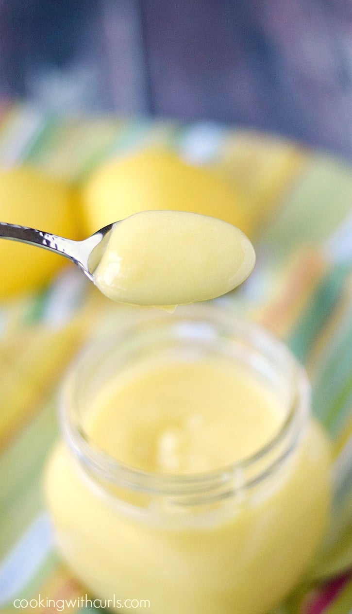 A spoonful of delicious Homemade Lemon Curd with lemons sitting on a striped napkin in the background