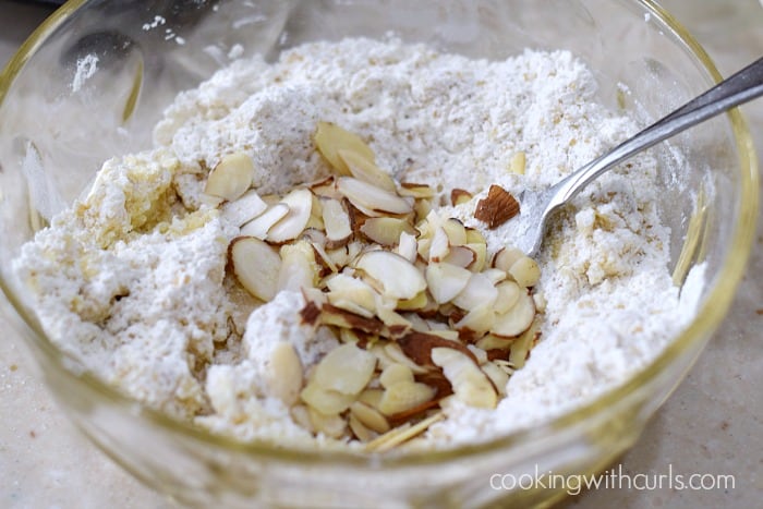Flour, butter, sugar, and sliced almonds mixed together in a glass bowl with a fork.