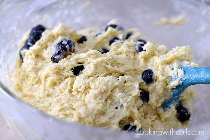 Fresh blueberries mixed into muffin batter with a silicone spatula.