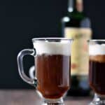 Two glass mugs filled with Irish Coffee sitting in front of a bottle of Jameson whiskey