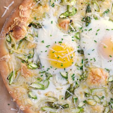 pizza topped with asparagus, cheese and sunny side up eggs on a brown sheet of parchment paper