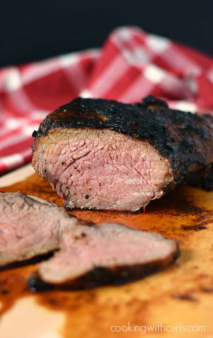 slices of tri-tip laying on a wood cutting board with a red and white check napkin in the background