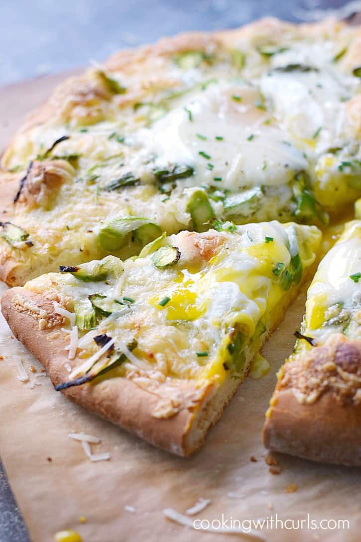 asparagus brunch pizza cut into slices and sitting on a sheet of brown parchment paper