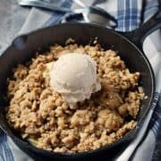 Mini cast iron skillet with apple crisp topped with vanilla ice cream.