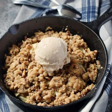 Mini cast iron skillet with apple crisp topped with vanilla ice cream.