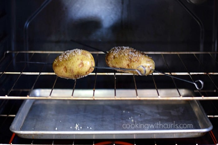 Two skewered potatoes inside an oven on the oven rack with an empty baking sheet on the rack below.