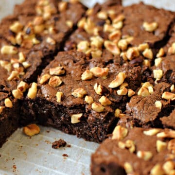 A pan of eight hazelnut brownies with chopped hazelnuts on top and one brownie removed.