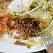 A shredded beef chimichanga cut open on a plate to show the filling topped with sour cream and shredded lettuce.