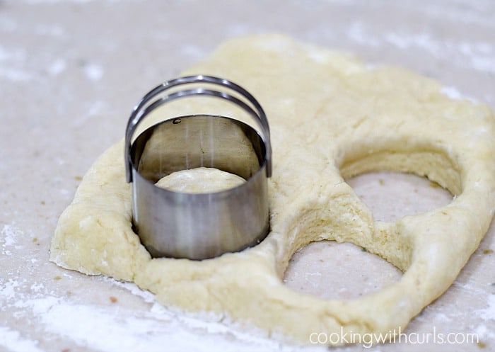 A thick rectangle of biscuit dough being cut with a round cutter on a floured work surface.