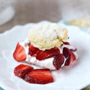 Sugar topped biscuit cut in half and filled with whipped cream and sliced strawberries on a dessert plate.