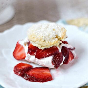 Sugar topped biscuit cut in half and filled with whipped cream and sliced strawberries on a dessert plate.