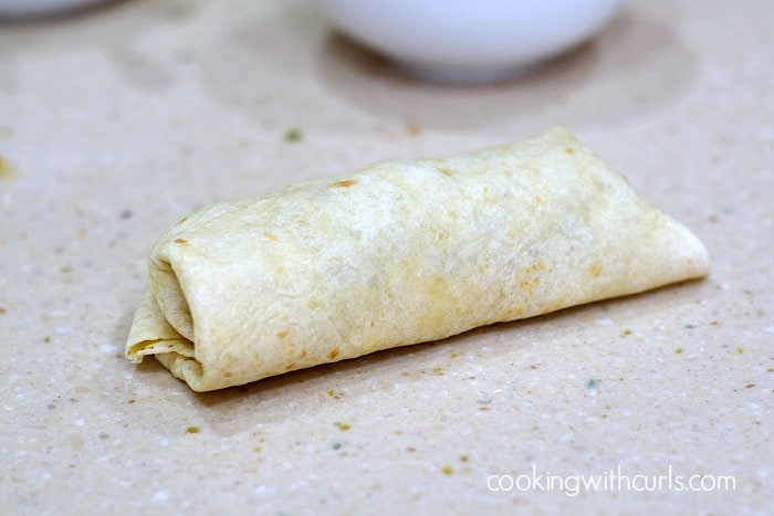 Flour tortilla rolled around shredded beef sitting on a counter top.