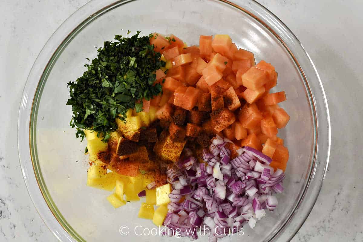 Chopped mango, papaya, onion, cilantro, lime juice, and chile powder in a mixing bowl.