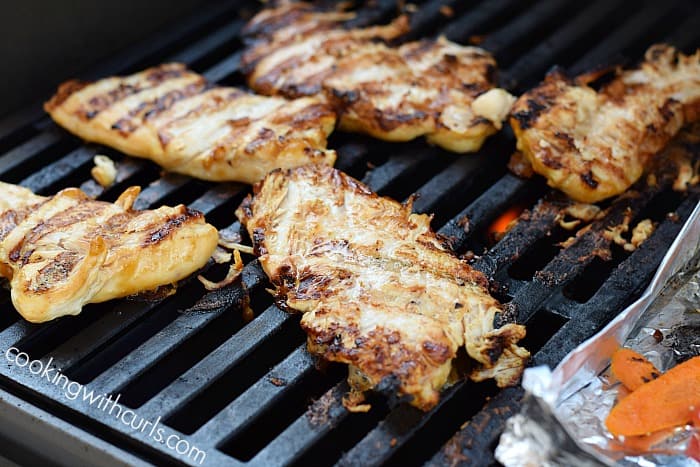 Five chicken breasts on a barbecue grill.