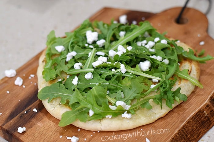 Grilled pizza topped with arugula leaves and crumbled goat cheese.
