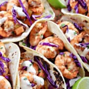 Four grilled shrimp tacos with papaya mango salsa on a wooden plate.