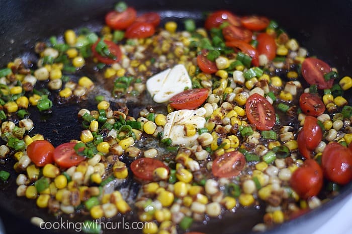 Corn, green onions, cherry tomato halves, and butter in a cast iron skillet.