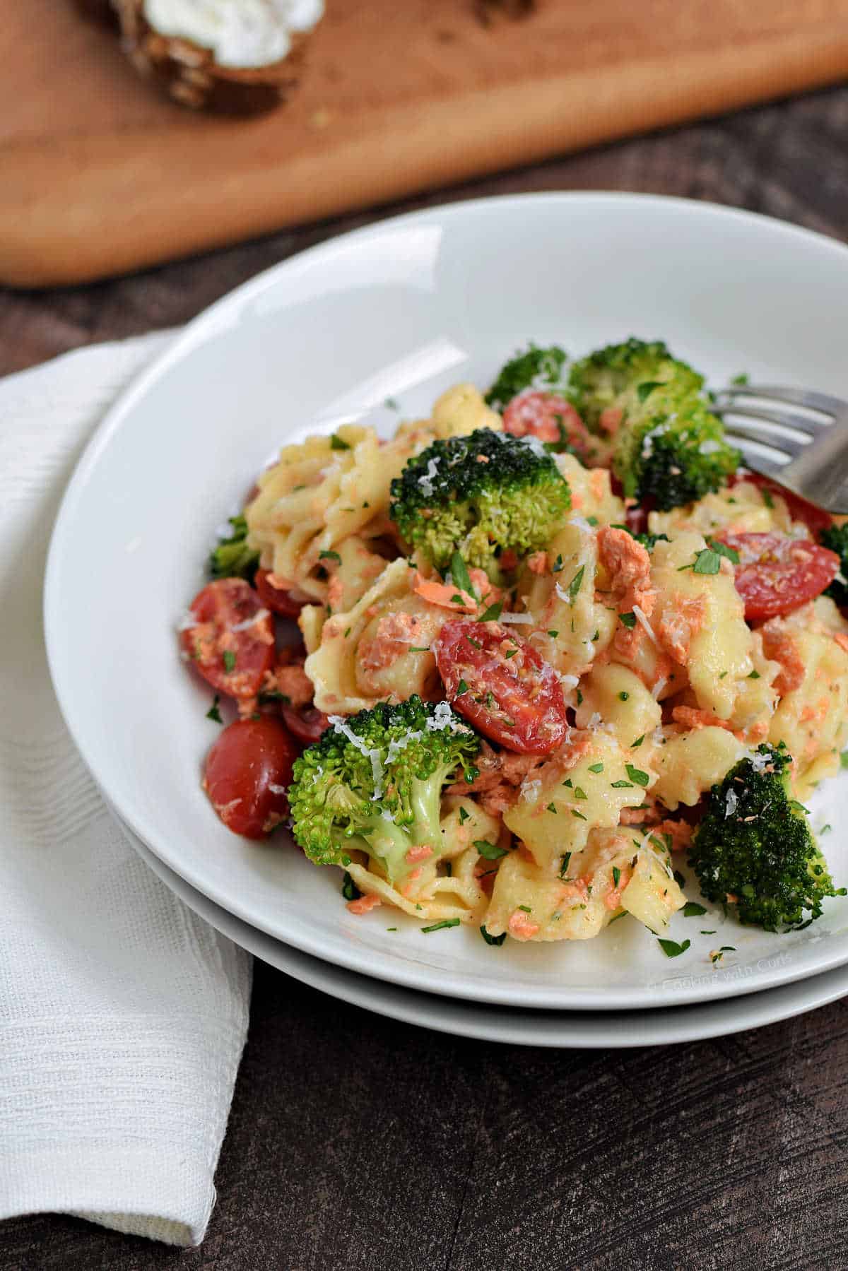 Tortellini, flaked salmon, broccoli florets and cherry tomatoes in a bowl.