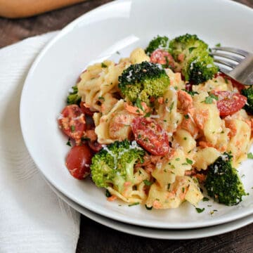 Cheese tortellini, broccoli and cherry tomatoes tossed in Italian dressing in a white bowl.