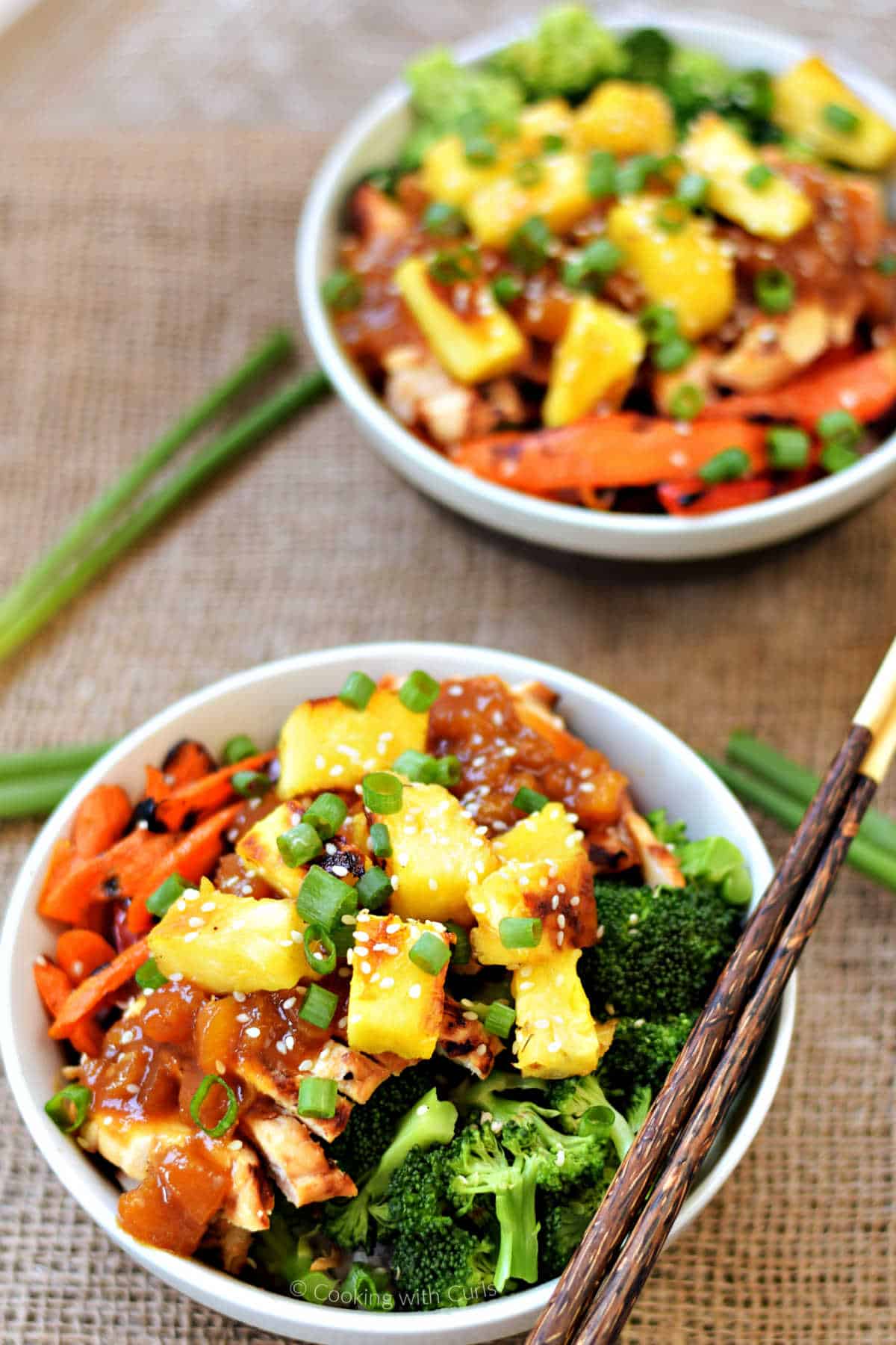 Two bowls of grilled chicken teriyaki and vegetables with chopsticks on the edge of the bowl.