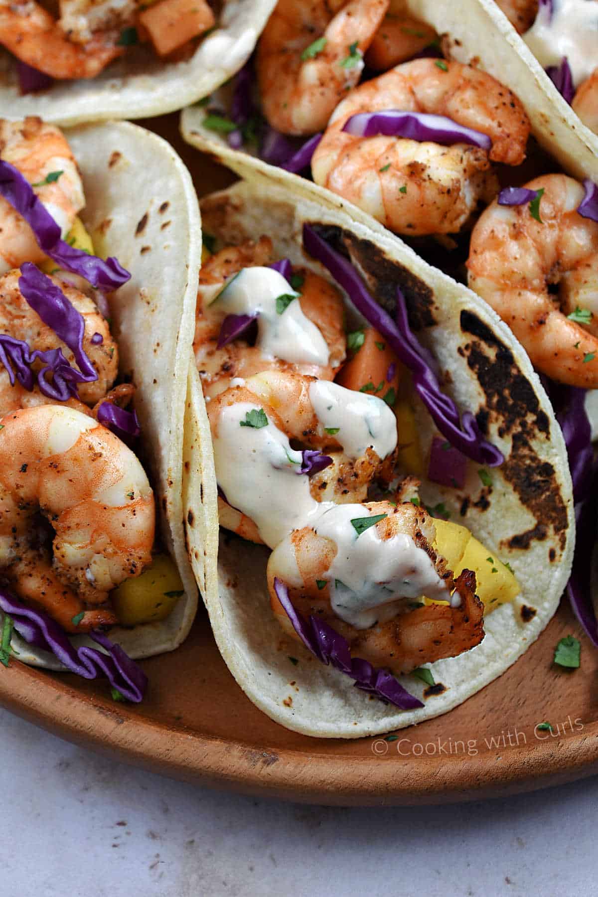 Grilled shrimp tacos topped with chipotle crema on a wooden plate.