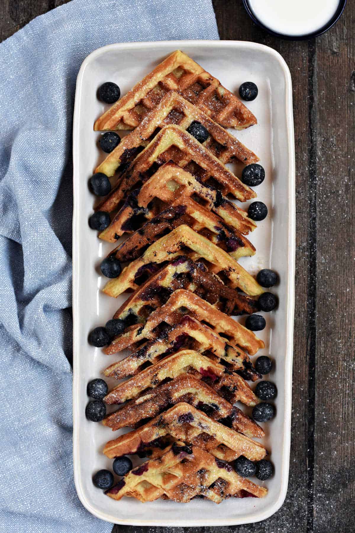 Blueberry Lemon Waffled Muffins cut into triangles on a platter with lemon glaze on the side.