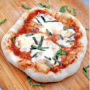 Puffy pizza topped with melted mozzarella and strips of basil on a wood pizza peel.