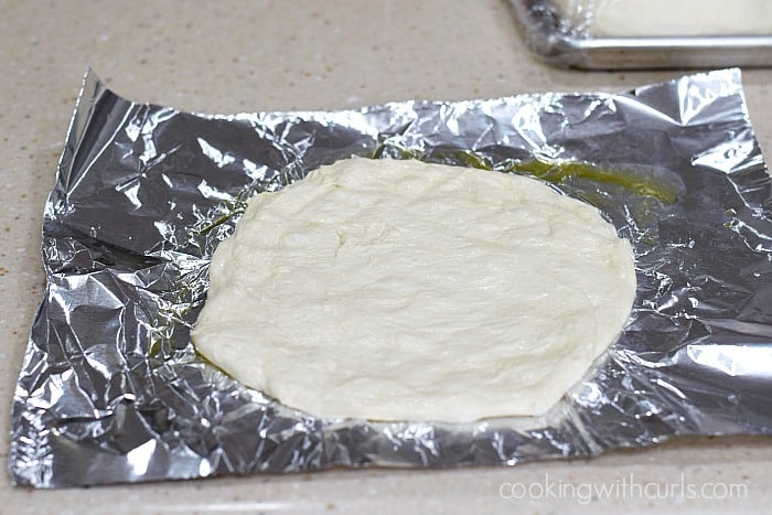 Oiled pizza dough round on a sheet of aluminum foil.