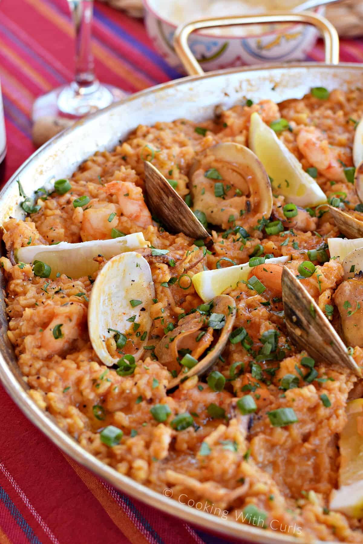 Rice, shrimp, clams and rice in a paella pan topped with sliced green onions.