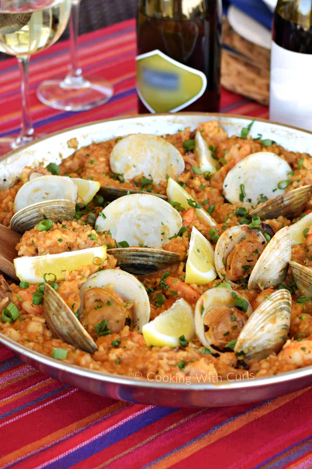 Rice, clams, shrimp, and cod in a paella pan with lemon wedges and green onions. 